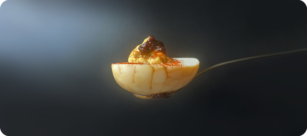 spoon holding a deviled tea egg against a black background